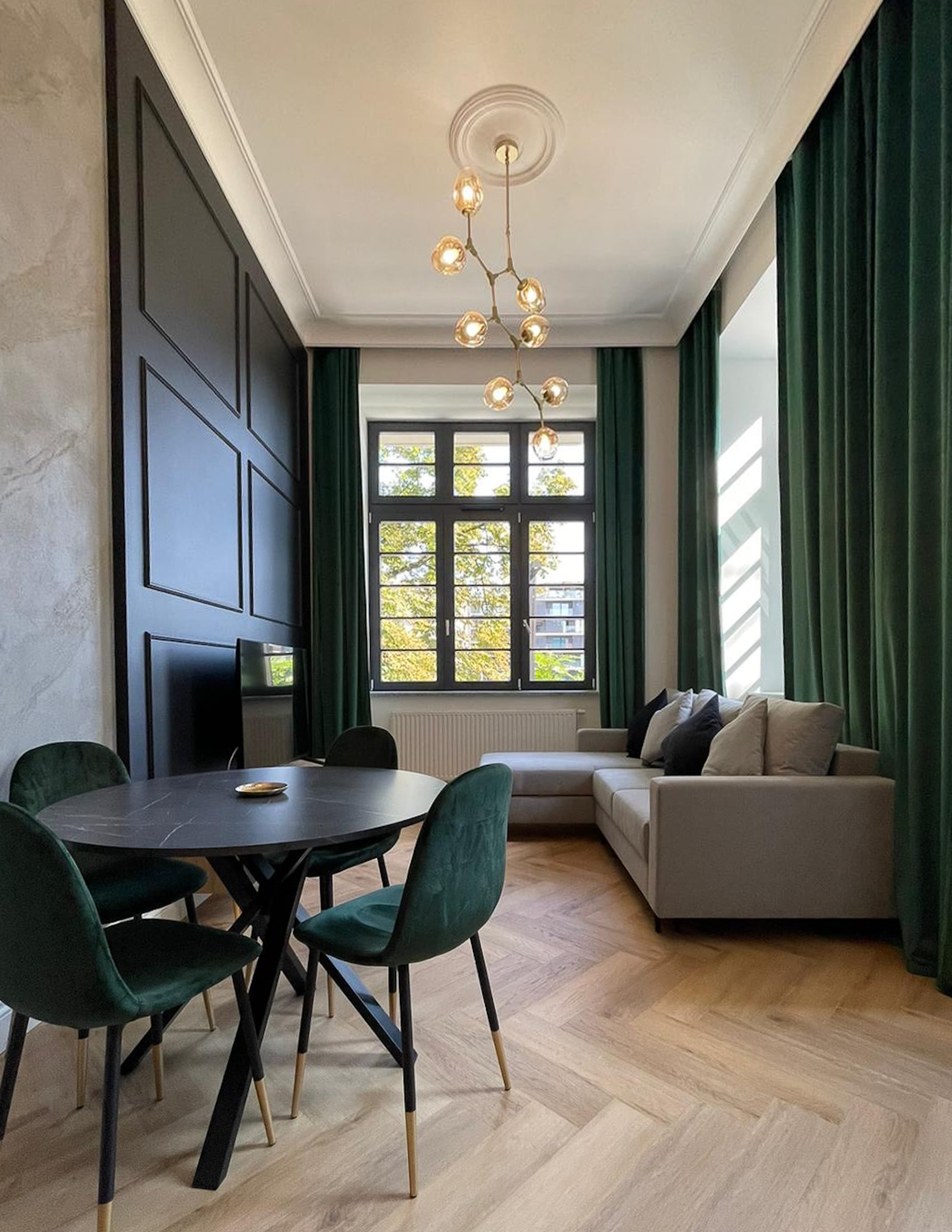 Nowoczesna aranżacja salonu z jadalnią, eleganckie zielone krzesła, czarny stół i szara sofa w stylowym wnętrzu