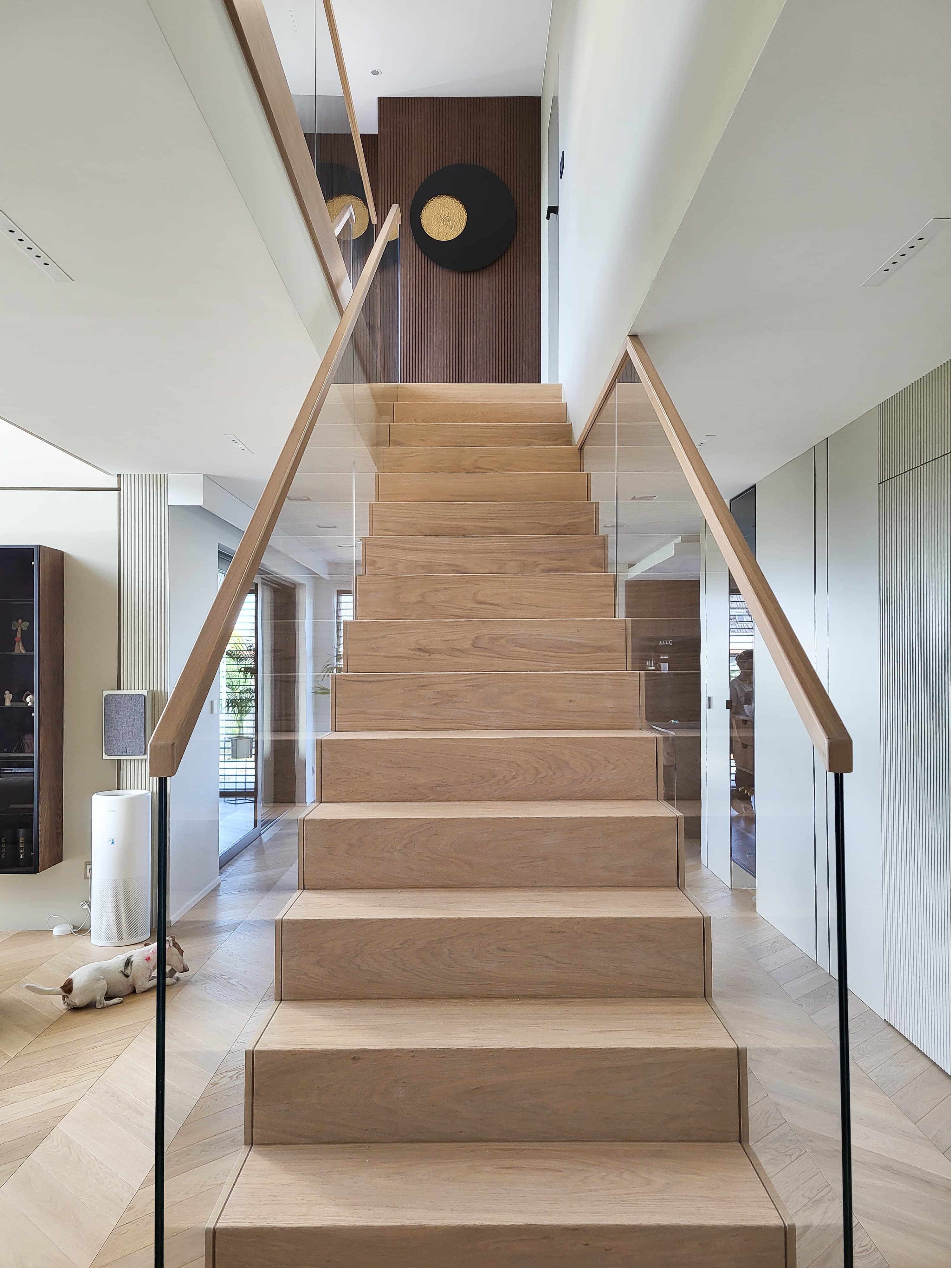 Nowoczesne schody drewniane z przeszkloną balustradą w eleganckim wnętrzu domu, z dekoracyjną ścianą w tle i designerskimi detalami